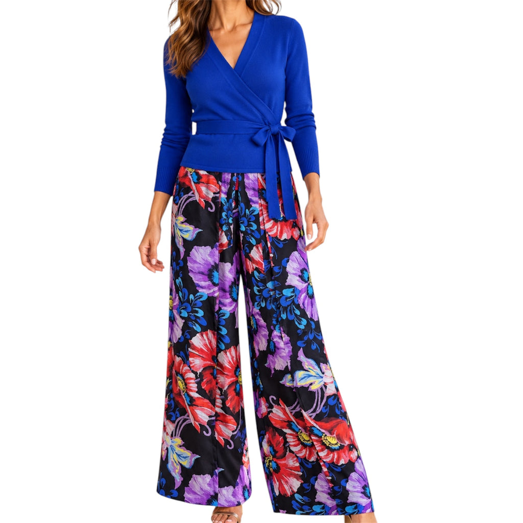 A woman modeling a royal blue cashmere long-sleeve wrap Cardigan with a tie waist and matching wide-leg silk floral pants featuring a vibrant multicolor print on a black background.