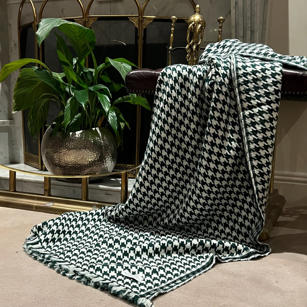 A houndstooth patterned 100% pure cashmere throw in hunter green and white, draped over a armchair in a living room setting.