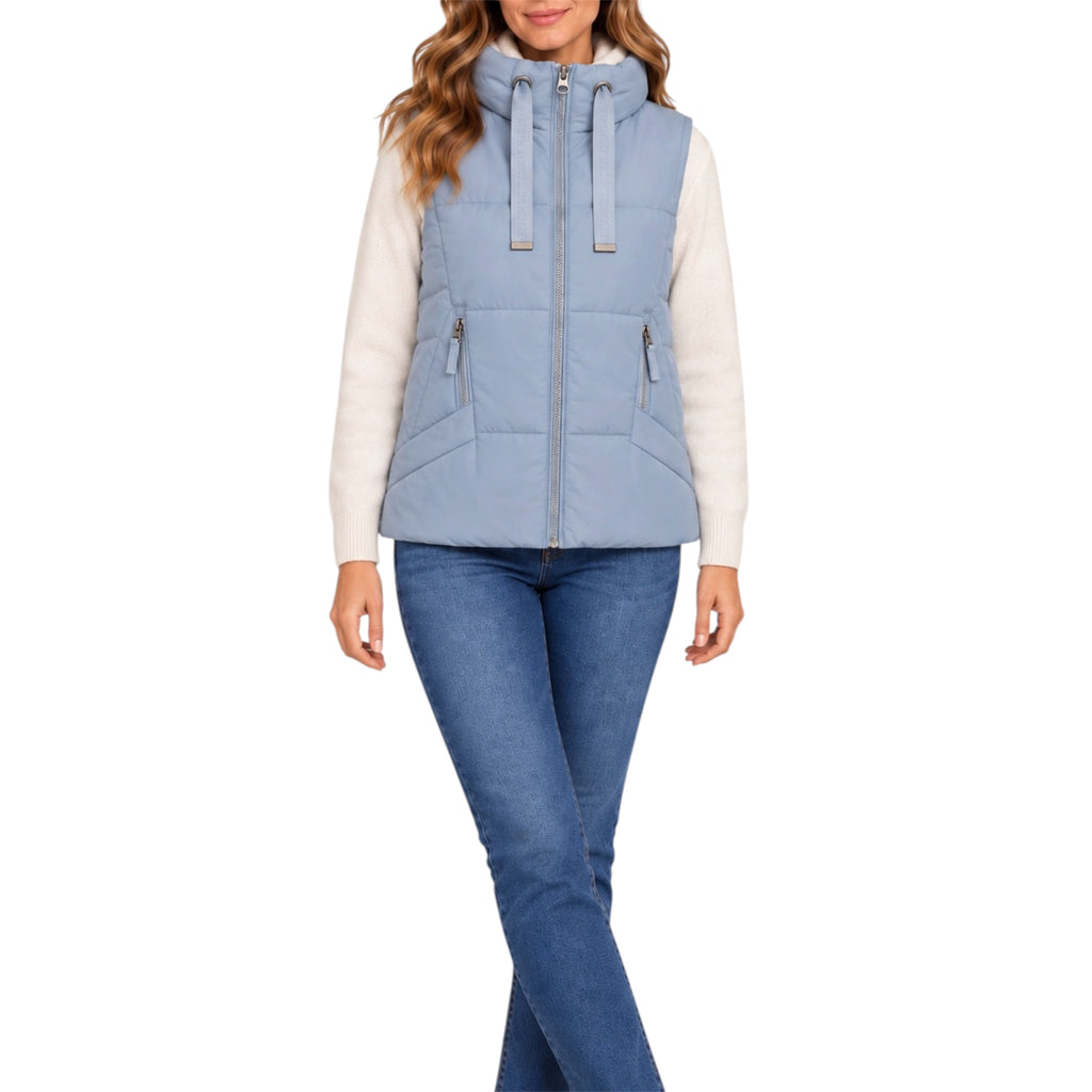 A woman wearing a light blue hooded puffer vest over a cream long-sleeve top and blue jeans, shown against a plain white studio background.
