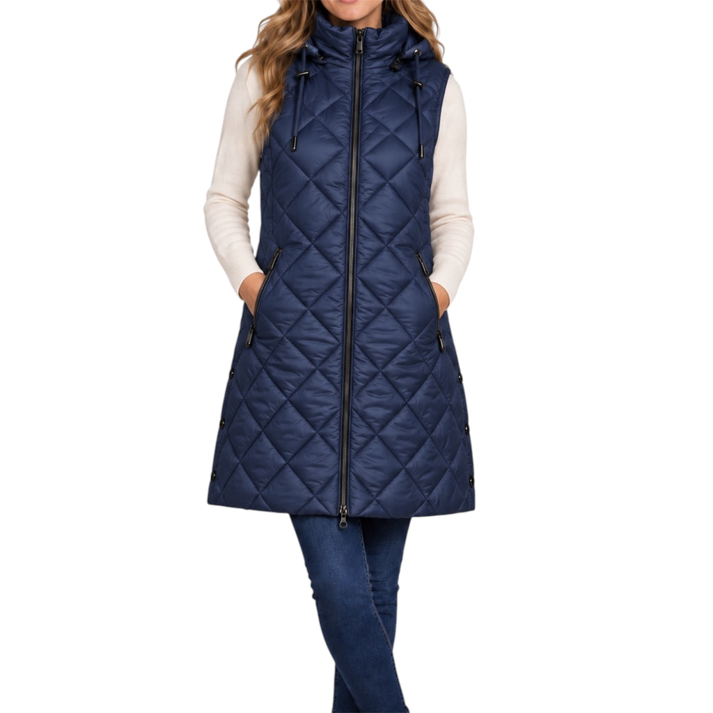 A woman wearing a navy blue quilted sleeveless puffer vest with a front zipper, drawstring hood, and side pockets, layered over a cream long-sleeve top and blue jeans, against a plain white background.